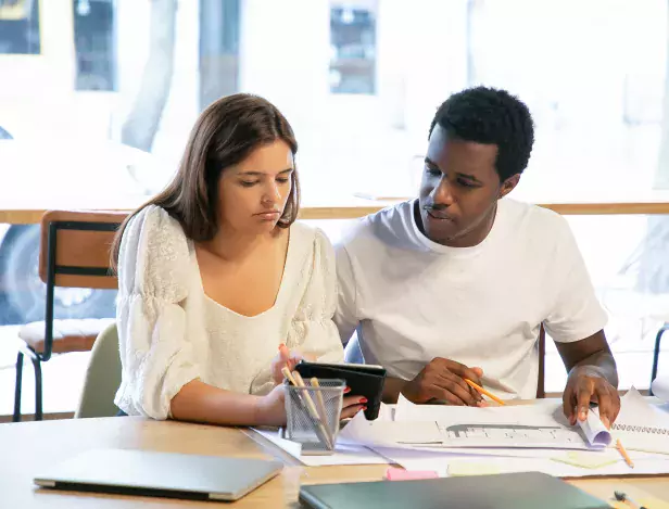 jeunes-designers-songeurs-regardant-plans-ecran-tablette-assis-table-travaillant-ensemble-parlant